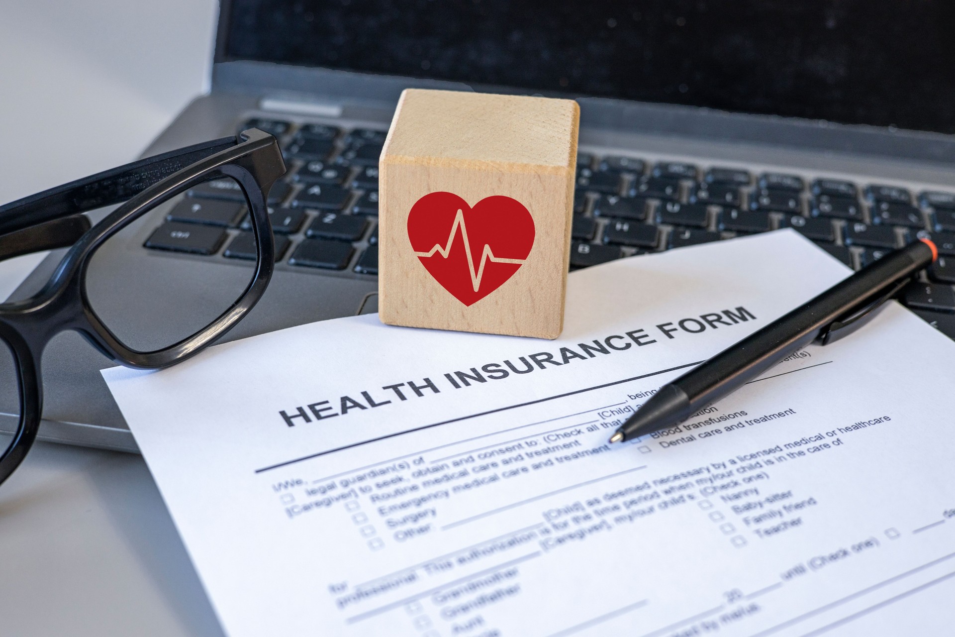 Health insurance policy. Health insurance form, red heart beat icon on wooden cube and computer on desk.